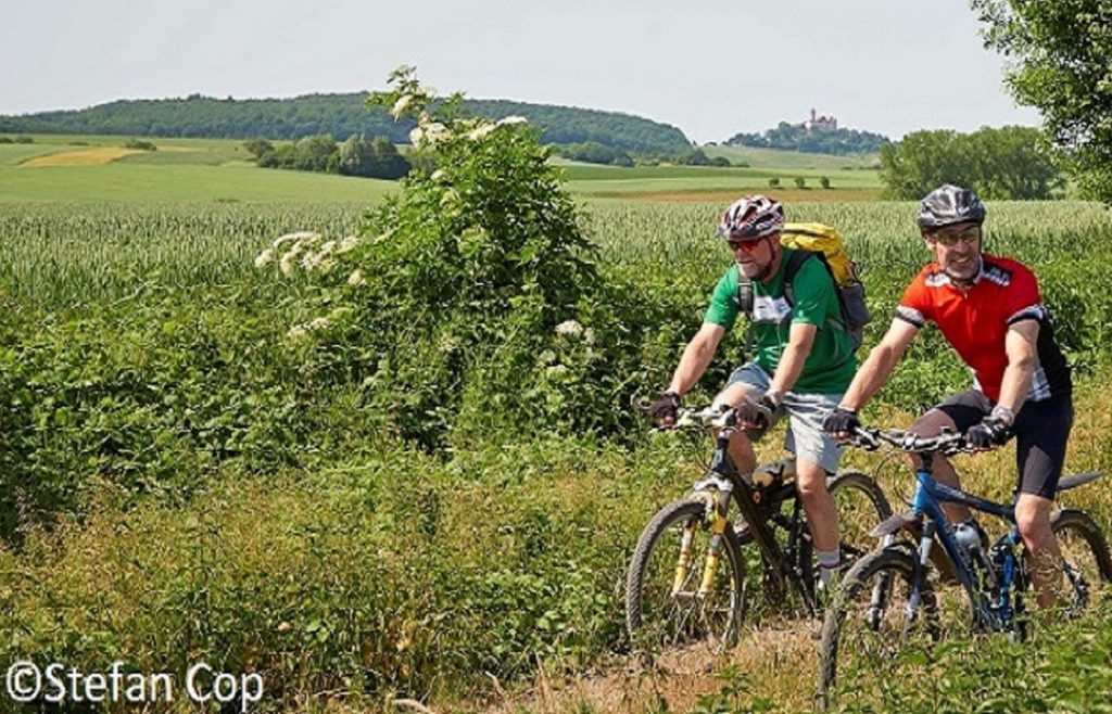 Zwei Radfahrer auf einem Feldweg, im Hintergrund Hügel