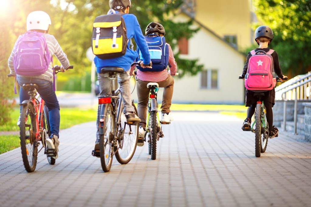 Children With Rucksacks Riding On Bikes In The Park Near School Bild einer Gruppe Kinder auf Fahrrädern